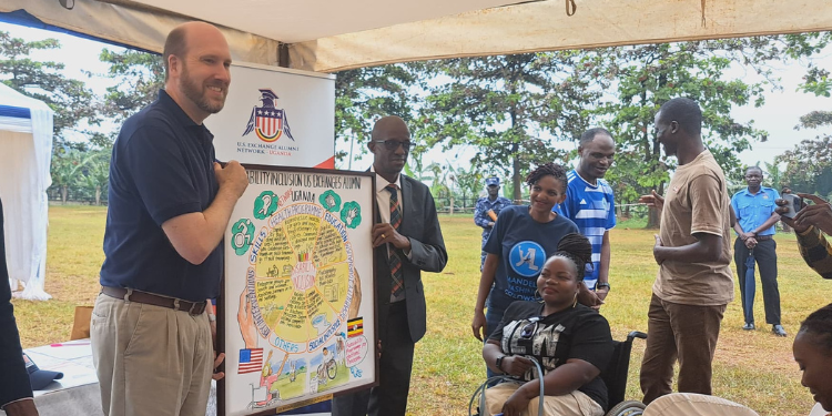 Ambassador William W. Popp poses with the Virtual Map that communicates the visions of the members of the U.S. Exchange Disability Inclusion Alumni Network - Uganda, alongside Professor Moses Muhwezi, Vice Chancellor of Makerere Business School. Looking on is Gorreti Byomwire (standing in a dark blue t-shirt), President of the U.S. Exchange Disability Inclusion Alumni Network - Uganda, and Josephine Namirimu (PFP Alumnus), member of the U.S. Exchange Disability Inclusion Alumni Network - Uganda.